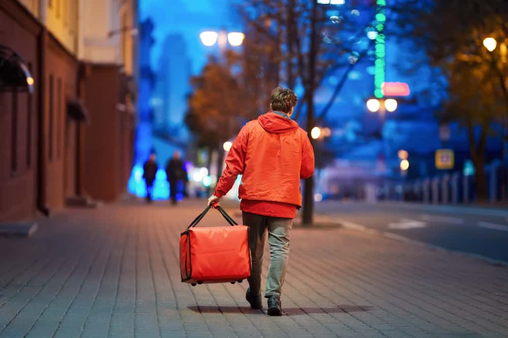 Young,Deliveryboy,Walking,With,Red,Thermal,Bag,On,Night,City