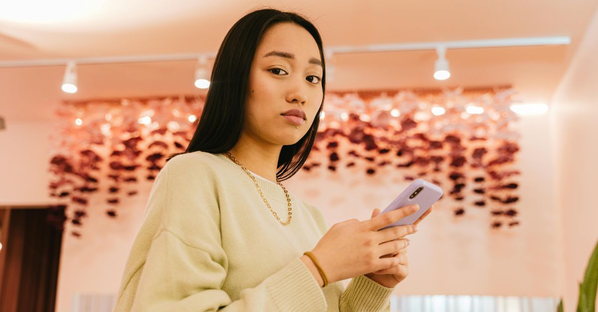 Woman in Sweater Holding a Smartphone and Looking at the Camera
