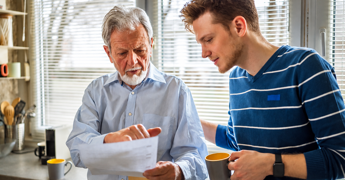 Senior father and adult son carefully going over documents in their kitchen
