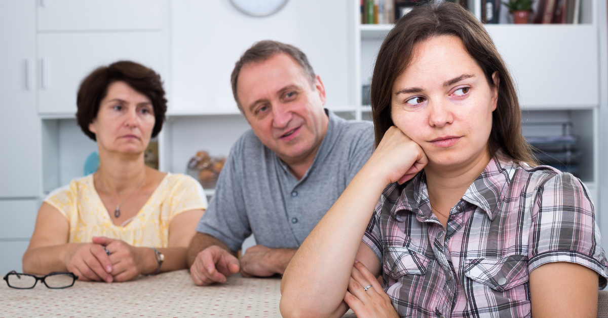 Young woman sitting and looking unhappy while talking with senior parents indoors
