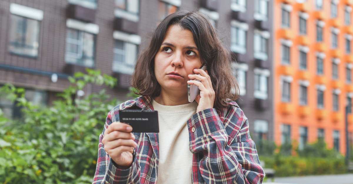 Woman standing outdoors, talking on the phone and holding a bank card