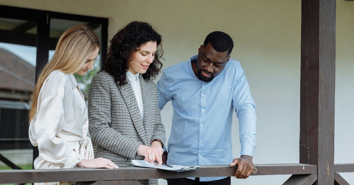 Real estate agent discussing property paperwork with a couple on a porch.