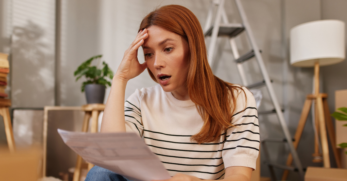 A woman sits on the floor surrounded by unpacked boxes and plants