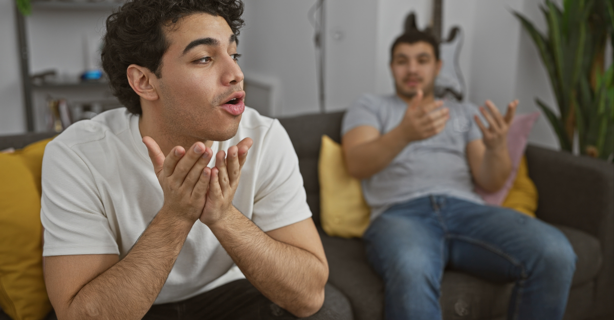 Two hispanic men having a lively discussion in a modern living room setting, expressing emotions and gestures.