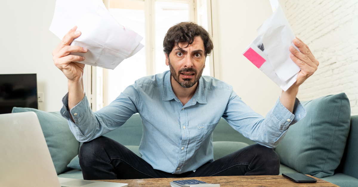 young angry and worried man working with laptop at home looking at bills and paying bills in home finance concept
