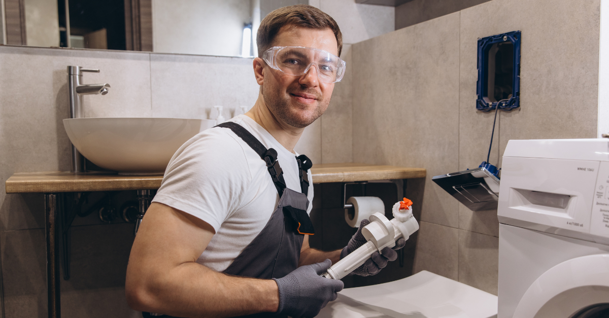 Plumber wearing safety glasses and gloves, holding a toilet fixture, working in a modern bathroom