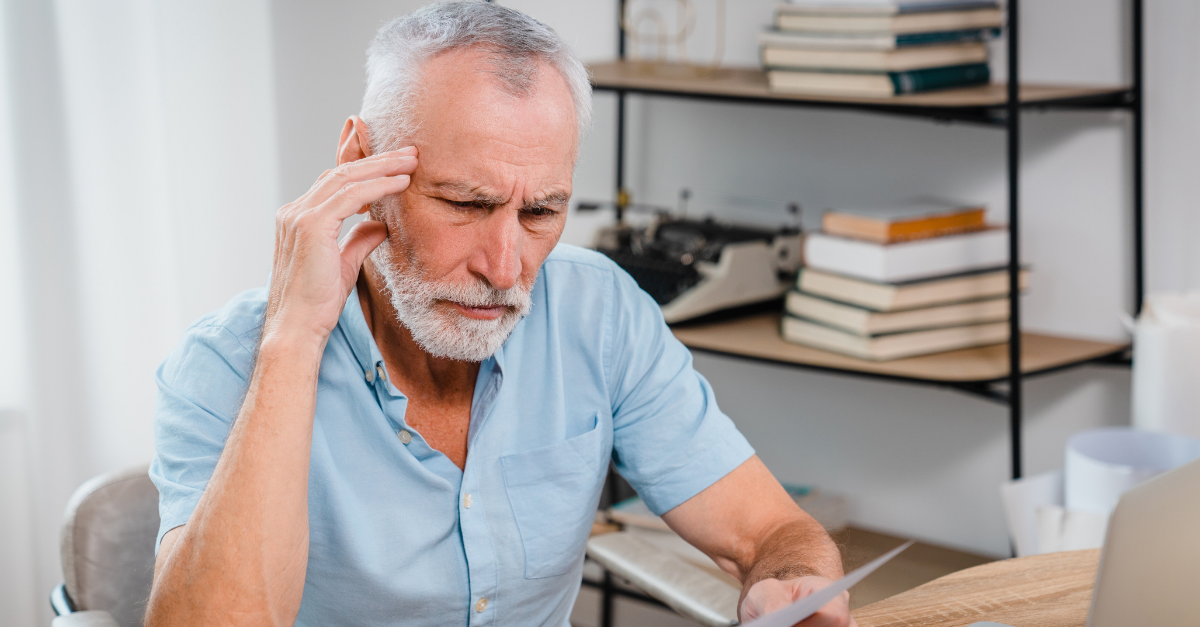 Serious mature man wearing glasses sitting on table home office