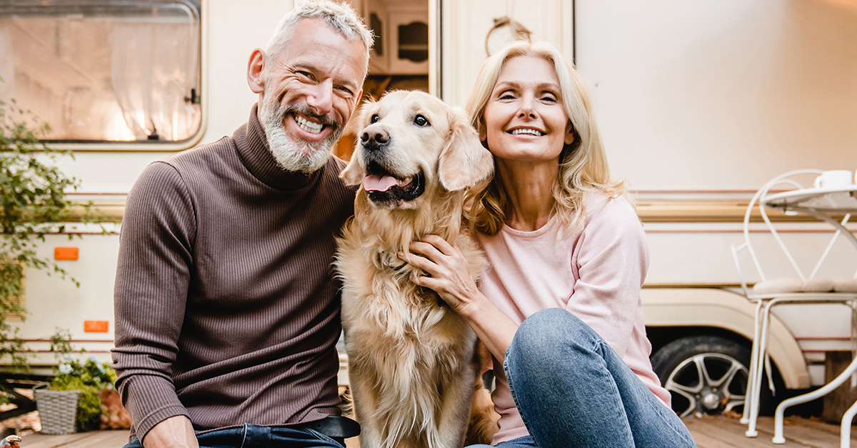 Happy senior caucasian couple spouses travelers explorers sitting in the garden near camper van trailer with their dog pet golden retriever with vegetables on the porch