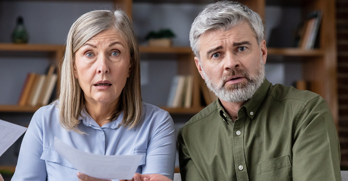 Senior couple sitting on sofa, holding documents and calculator, having shocked and stressed expressions while dealing with financial problems and high bills