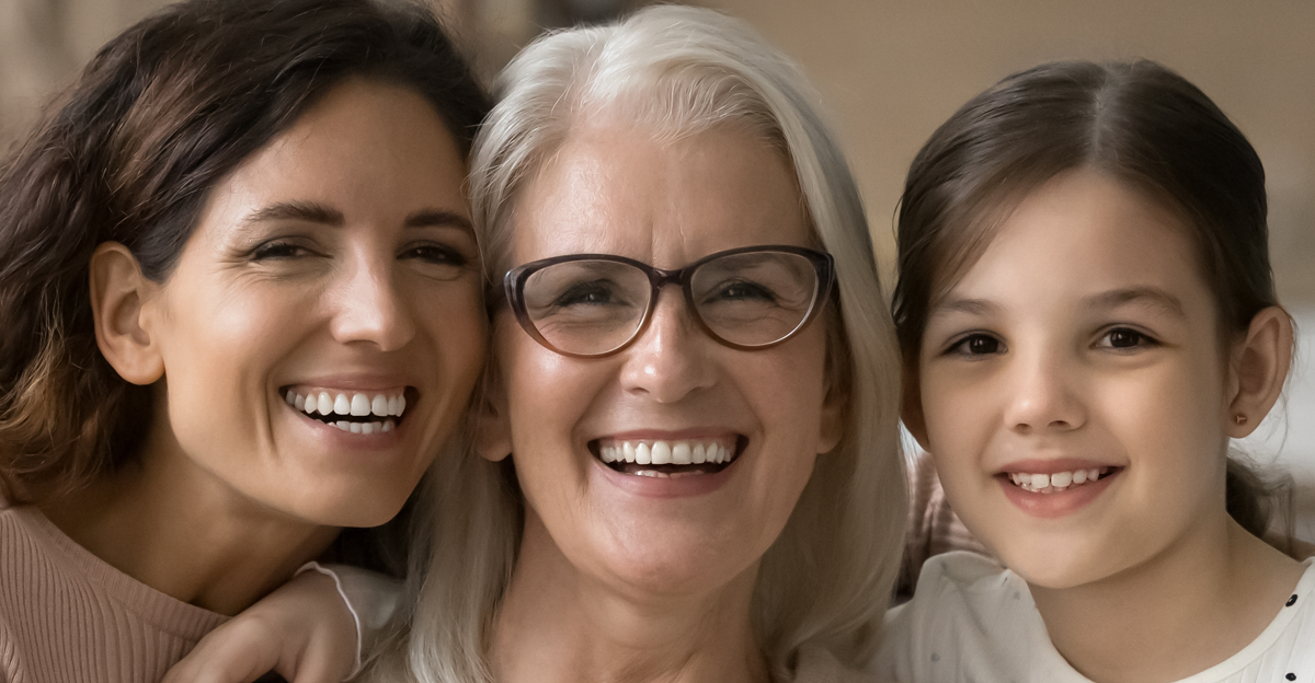 Happy grandma, mom and granddaughter kid sitting close on home sofa.