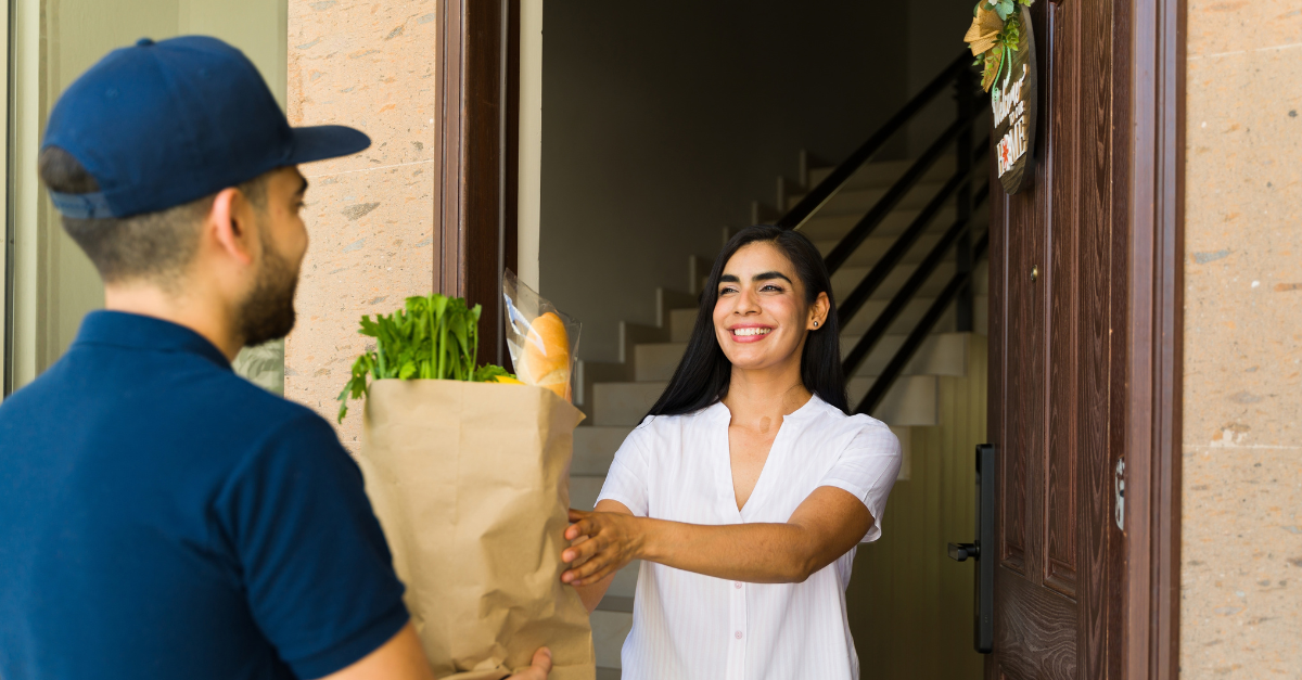 Cheerful woman is receiving a grocery bag from a delivery man in front of her house