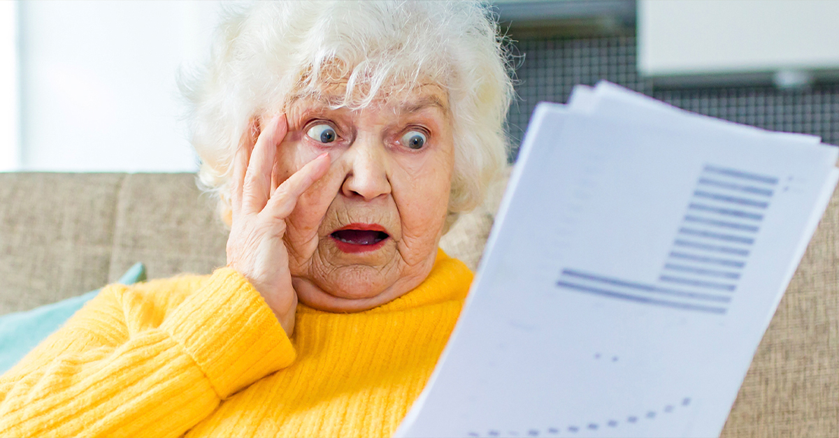 shocked amazed old woman white gray-haired sitting on the sofa in living room with laptop and bills